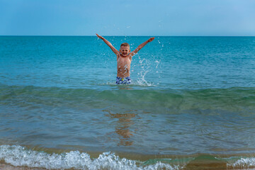 A boy swims in the sea on a sunny day. The child rejoices and splashes in the water.