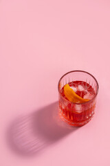 Negroni cocktail with orange peel on pink background with a shadow