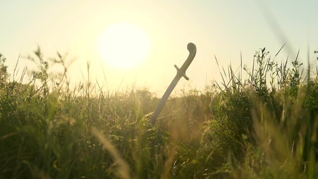 The saber of the Ukrainian Cossacks is stuck in the ground, among the grass, against the background of the sunset. The camera moves to the grass. The concept of freedom.