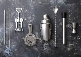 Various bar cocktail stainless steel utensils set on black stone background.