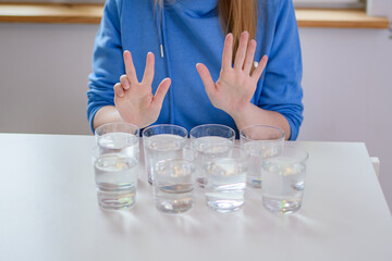 Fototapeta na wymiar Osiem szklanek wody na stole i dziewczyna w niebieskiej bluzie