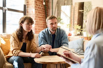 Young couple holding hands and supporting each other during conversation with psychologist