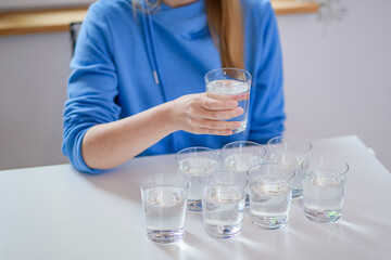 Kobieta pije wodę, przed nią stół na którym stoją napełnione szklanki - obrazy, fototapety, plakaty