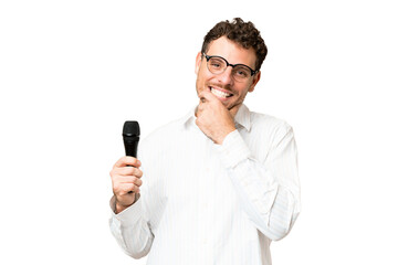 Brazilian man picking up a microphone over isolated chroma key background happy and smiling