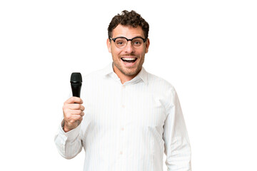 Brazilian man picking up a microphone over isolated chroma key background with surprise facial expression