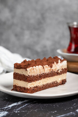 Traditional italian dessert tiramisu cake. Slice of chocolate cake with tiramisu cream and cocoa powder on dark table.