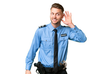 Young police man over isolated background listening to something by putting hand on the ear