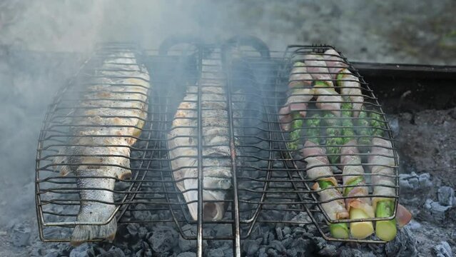 Grilling sea bass fish and asparagus on grill. Summer time on backyard. Food video