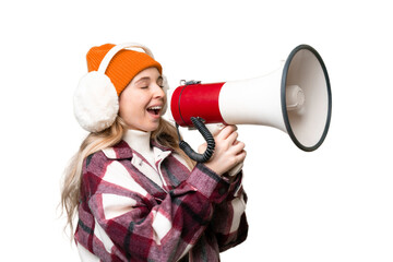 Young  English woman wearing winter muffs over isolated background shouting through a megaphone