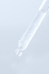 Naklejka na ściany i meble Dropper pipette pouring transparent liquid on light blue background .
