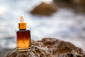Obraz na płótnie Canvas Bottle with essential oil or face skin moisturizer serum on rock in the sea background 