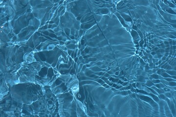 Blue water with ripples on the surface. Defocus blurred transparent blue colored clear calm water surface texture with splashes and bubbles. Water waves with shining pattern texture background.