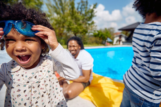 Joyful Afro-American Girl in Snorkeling Goggles, Supported by Smiling Father and Brother by the Poolside
