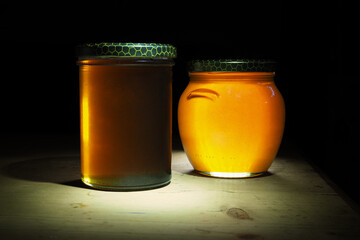 two jars of honey illuminated by light with a black background