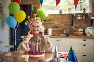 Joyful happy lovely senior woman wearing inflatable crown celebrating birthday alone at home, feeling happy.