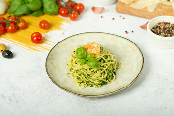 Pasta spaghetti with pesto sauce and fresh basil leaves in grey bowl. Light grey background