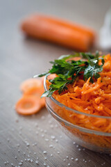 Bowl with fresh grated carrot and oil background.