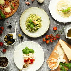Full table of italian meals on plates Pizza, pasta, ravioli, carpaccio. caprese salad and tomato bruschetta on black background.