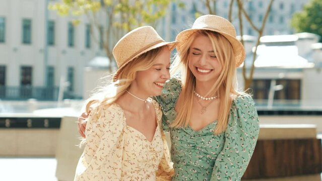 Two young beautiful smiling hipster female in trendy summer sundress clothes and straw hats. Sexy carefree women walking in street. Positive models having fun, hugging and laughing at sunny day