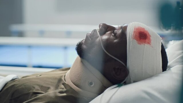 African American sick soldier with bleeding head wound lying on bed and looking at ceiling in military hospital