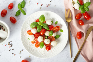 Italian caprese salad with sliced tomatoes, mozzarella, basil, olive oil on a light background.