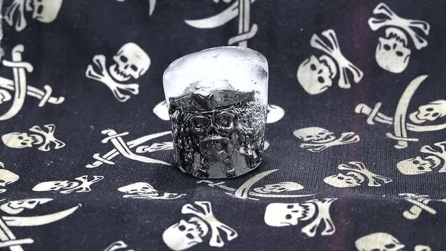 A ring in the form of a pirate skull in a hat and beard is thawed out of ice in a close-up time-lapse video