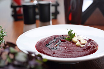 Beetroot cream soup, decorated with cheese, arugula and balsamic vinegar, in a white bowl, close-up.