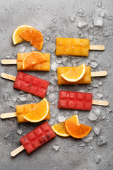 Colorful orange and watermelon popsicles with crushed ice and orange slices on gray stone background. Healthy summer food concept. Top view, flat lay