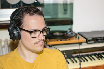 Young man with glasses enjoying while listening his vinyl record with vintage earphones in his room