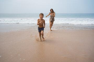 Fototapeta na wymiar Beautiful mother with son run at beach after swimming in sea at sunny day