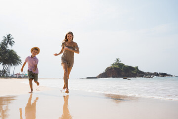 Beautiful young mother and son run at beach in sunny day and hugging