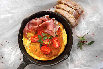 Omelette with tomato and prosciutto on a cast iron pan. Fresh vegetarian breakfast, top view,...