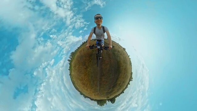 Smiling man in sunglasses rides cross-country mountain bicycle along path in field. 360 degrees action camera shot, tiny planet projection, Fisheye lens. Trip journey with MTB bike. Sports recreations