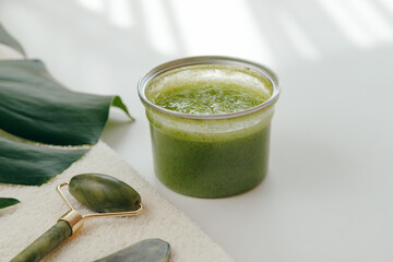 Green Sugar Body Polish Exfoliator in jar and Face Massage Accessories on white background, flat lay, top view.