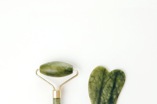 Facial jade massage rollers and gua sha massagers made from green quartz stone on white background