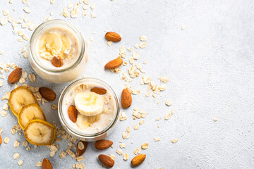 Almond banana smoothie with oat flakes in glass jars at white stone table. Top view.