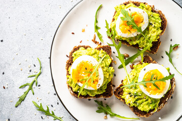 Open sandwich. Whole grain bread with avocado and boiled eggs. Top view on white kitchen table.