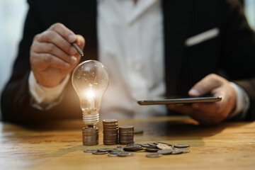 businessman holding a light bulb Concept of saving money with hands putting coins on wooden table floor