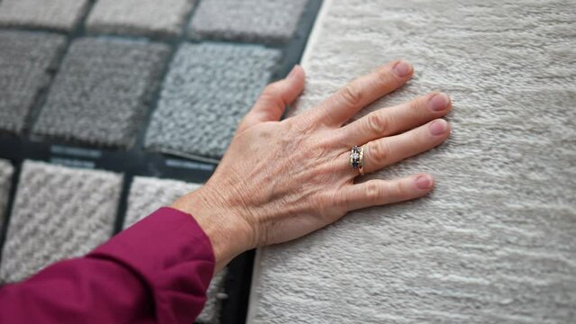 Closeup of mature womans hand moving across carpet or rug samples in a hardware store.