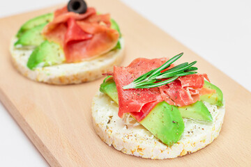 Rice Cake Sandwich with Avocado, Jamon, Olives and Rosemary on Wooden Cutting Board. Easy Breakfast. Quick and Healthy Sandwiches. Crispbread with Tasty Filling. Healthy Dietary Snack