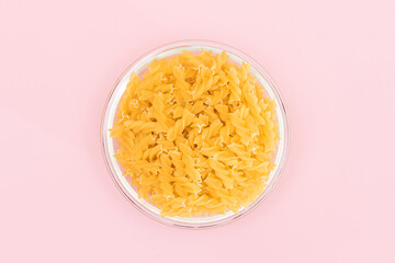 Uncooked Fusilli Pasta in Glass Jar on Pink Background. Fat and Unhealthy Food. Classic Dry Spiral Macaroni. Italian Culture and Cuisine. Raw Pasta