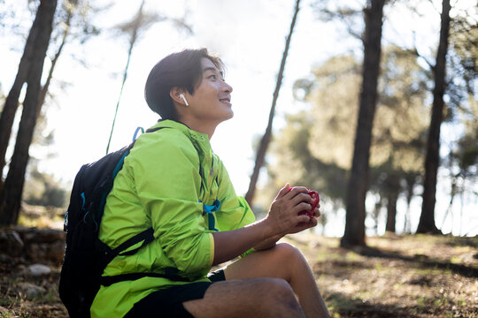 A young Korean man is sitting in the middle of the mountain while having a cup of coffee happily. Concept of Asians hiking, have breakfast outdoors.Copyspace