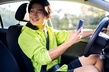 A young Korean man is using his mobile phone while driving a car. The boy looks back with a wink. Concept of recklessness at the wheel, avoidable accidents. Danger on the road.