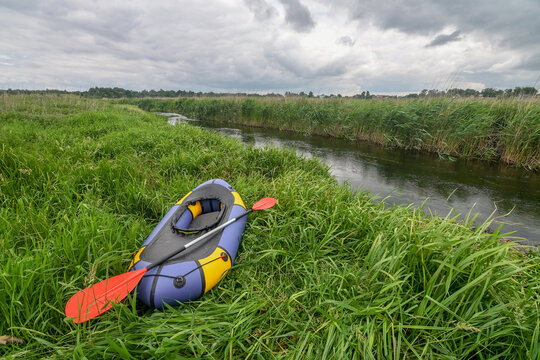 Multicolored packraft rubber boat on river bank, with dramatic sky. Selective focus. Active lifestyle concept.