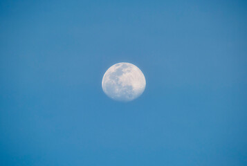 Naklejka na ściany i meble Bright full moon on blue sky during daylight. Round lunar disc