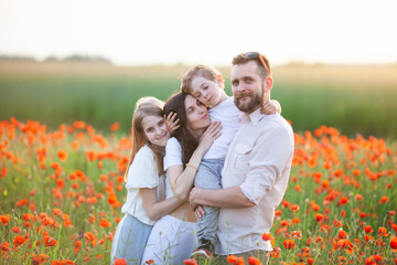 Happy family wearing white clothes hugging at the poppy field at sunrise. Mother, father, daughter and little son. Unity with nature, natural cosmetics, happiness concept. Selective focus.