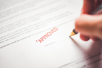 Close up of applicant signer holding pen to sign signature on official document paper with red...