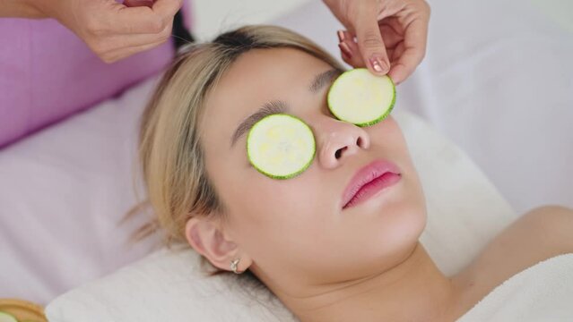 Close up face of beautiful young asian woman lying on spa bed while relaxing with fresh cucumber slices on eyes. Wellness and beauty health concept