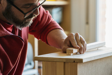 Closeup of a carpenter's hand assembling timber. Man with beard and glasses buiding a piece of...