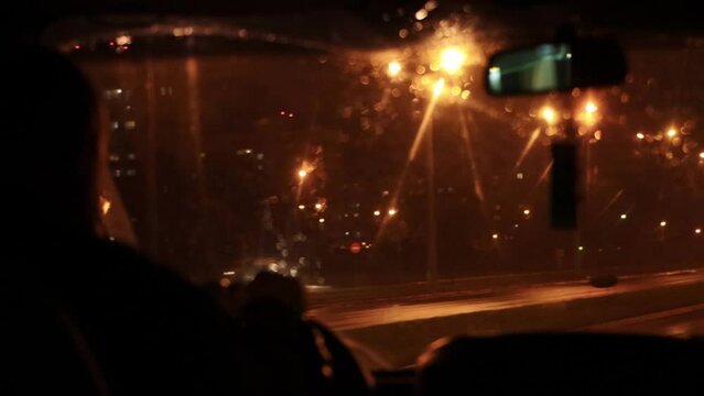 View from the car interior on a wet windshield in the rain at night. Poor visibility, bad weather conditions while traveling. Lights from the headlights of cars and lanterns. Copy space for text. Blur
